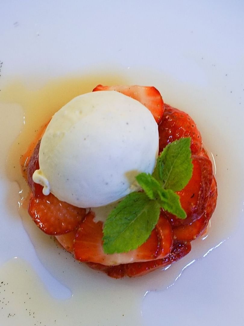 Sliced strawberries with a scoop of ice cream placed by a mint sprig on a plate at Warwick Grand Place Brussels
