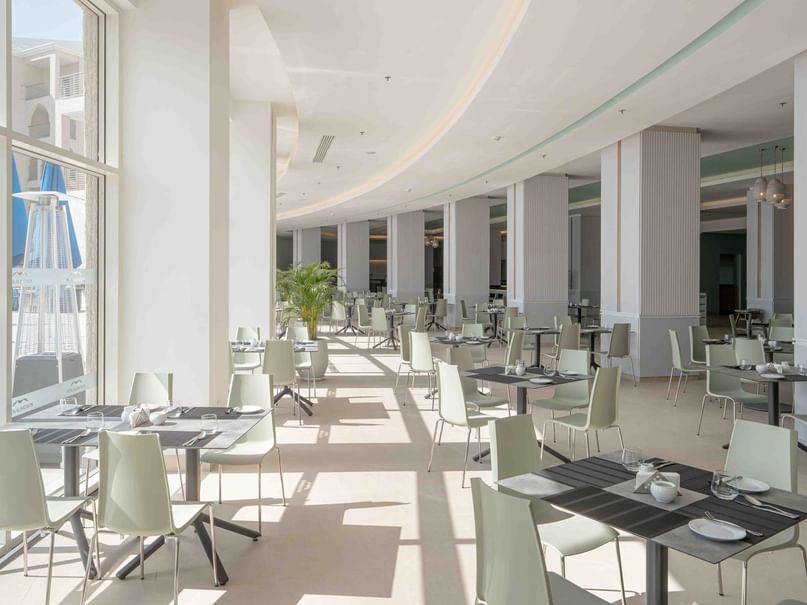 A modern, large, empty restaurant with many tables and chairs, large windows, and a curved ceiling.