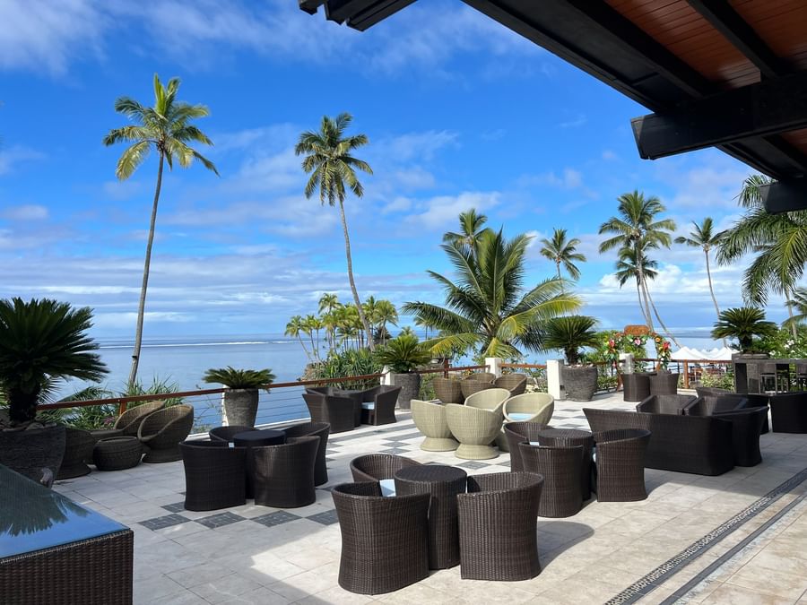 Outdoor seating area with ocean view and palm trees at Warwick Fiji Resort and Spa.