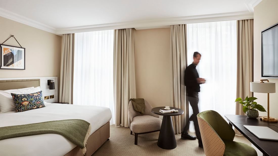 Man walking past a bed in Deluxe Room at The Clermont Victoria
