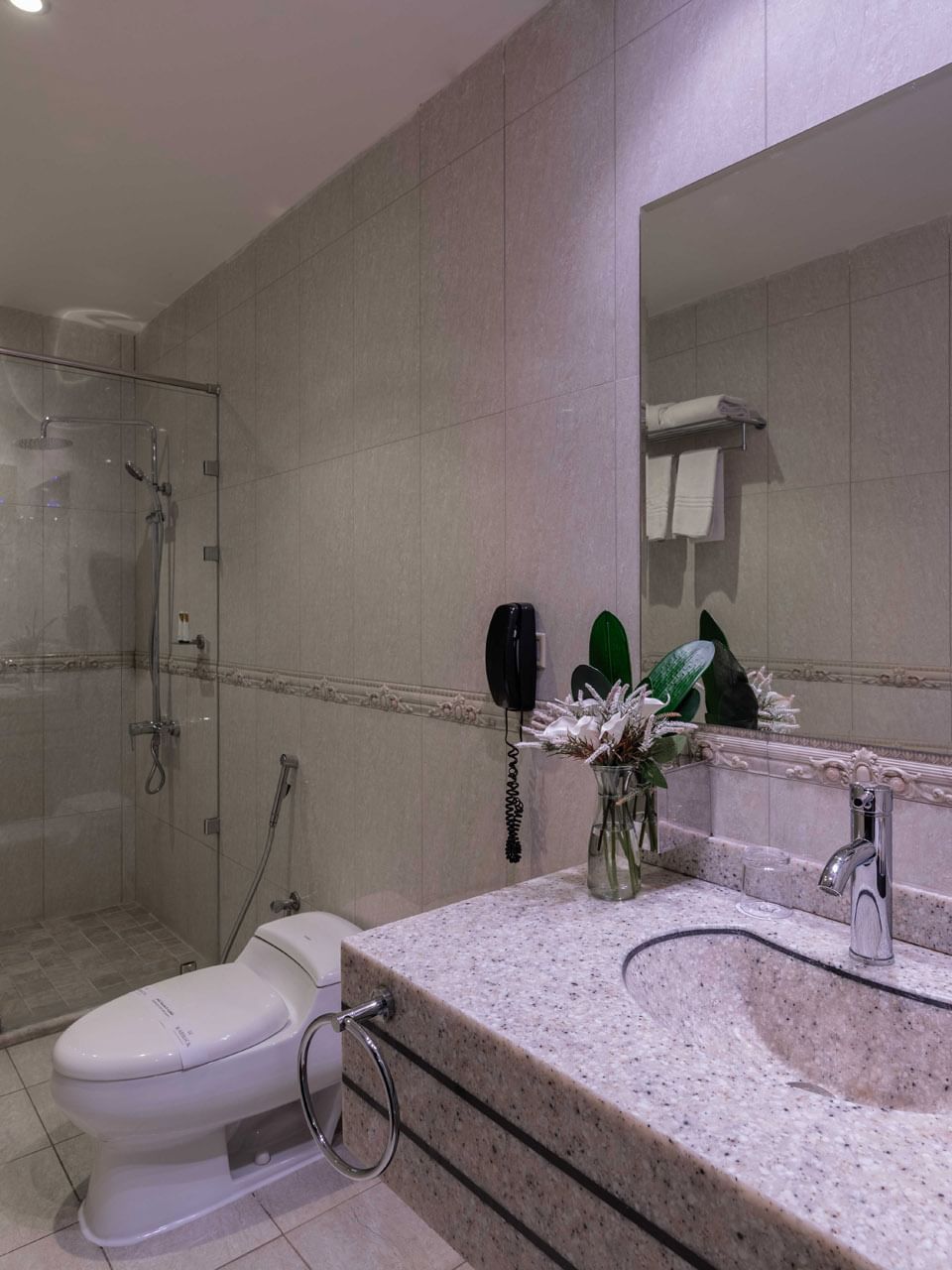 Granite vanity by a white toilet & a glass shower with a towel on handle in Junior Suite City View at Warwick Al Jubail