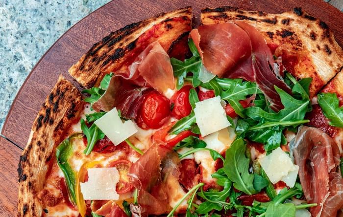 Artisanal pizza topped with prosciutto and arugula on a wooden board served at Anaheim Portofino Inn & Suites