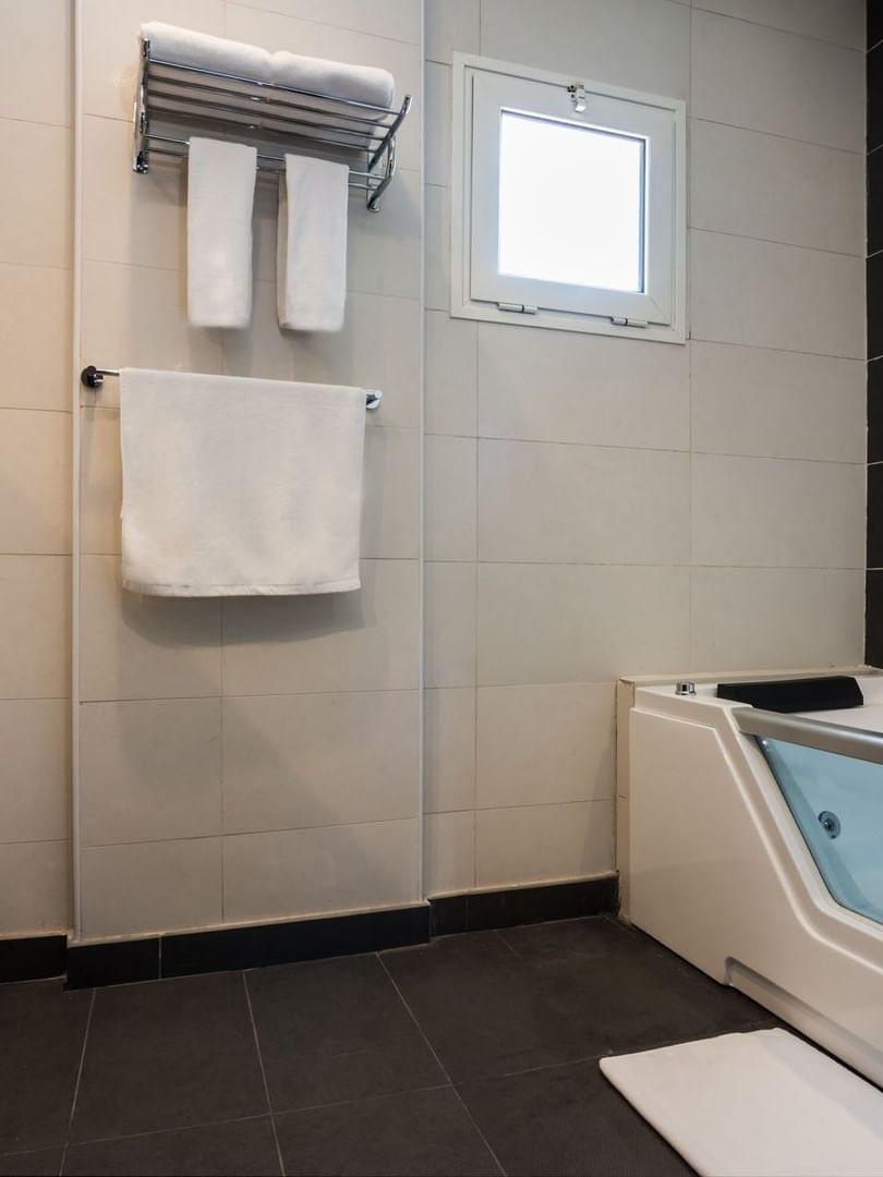 Executive Suite bathroom featuring a glass-front tub with a towel rack under a small window at Naviti By Warwick Dammam