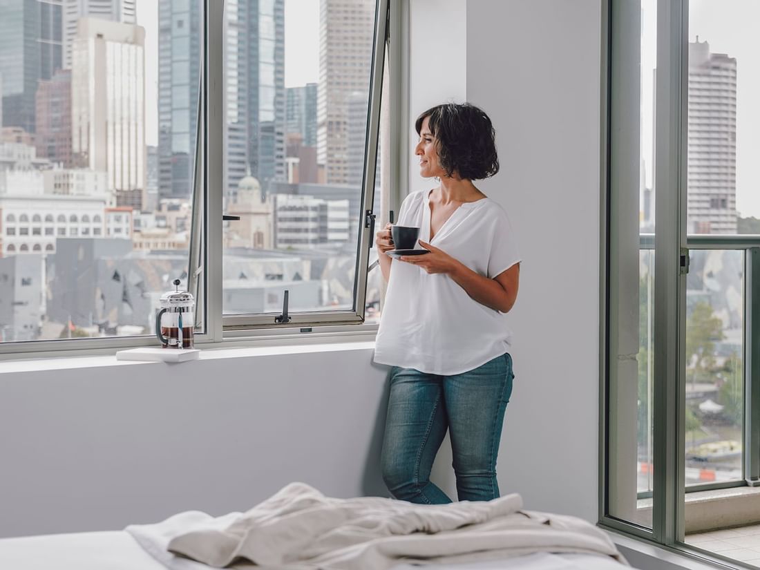 Lady standing by the window in 1 Bedroom Deluxe Apartment with City & River Views at Quay West Suites Melbourne