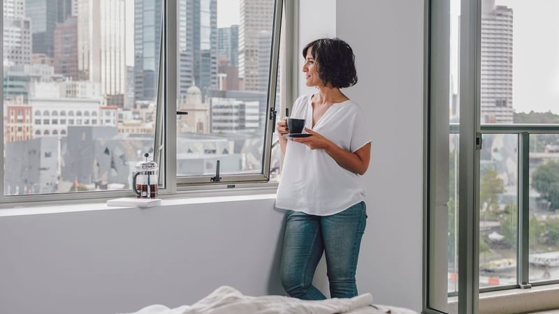 Lady standing by the window in 1 Bedroom Deluxe Apartment with City & River Views at Quay West Suites Melbourne