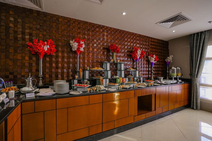 Long buffet counter with various food dishes, set against a dark wood block wall at Saja Warwick Madinah