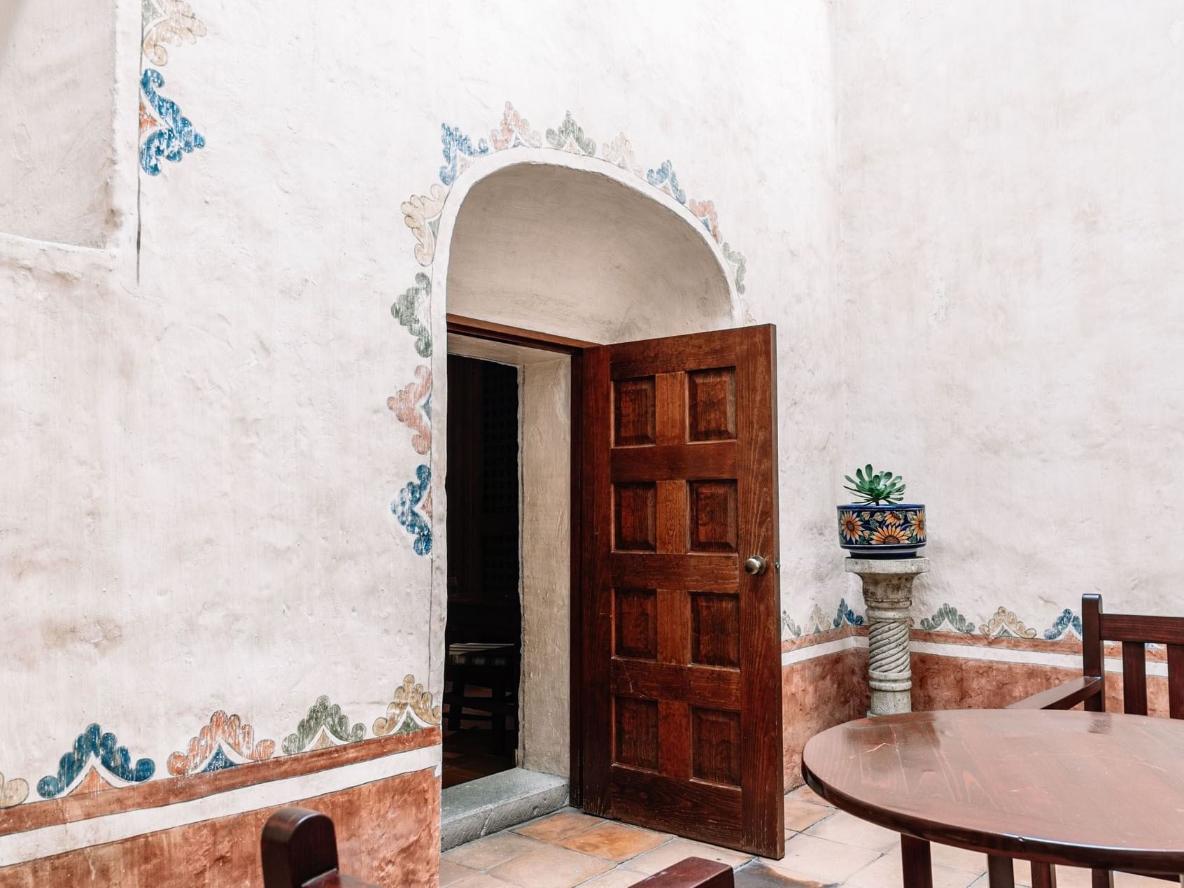 Wooden door slightly ajar in a white stucco wall, adorned with floral designs in King Governor Suite at Quinta Real Oaxaca