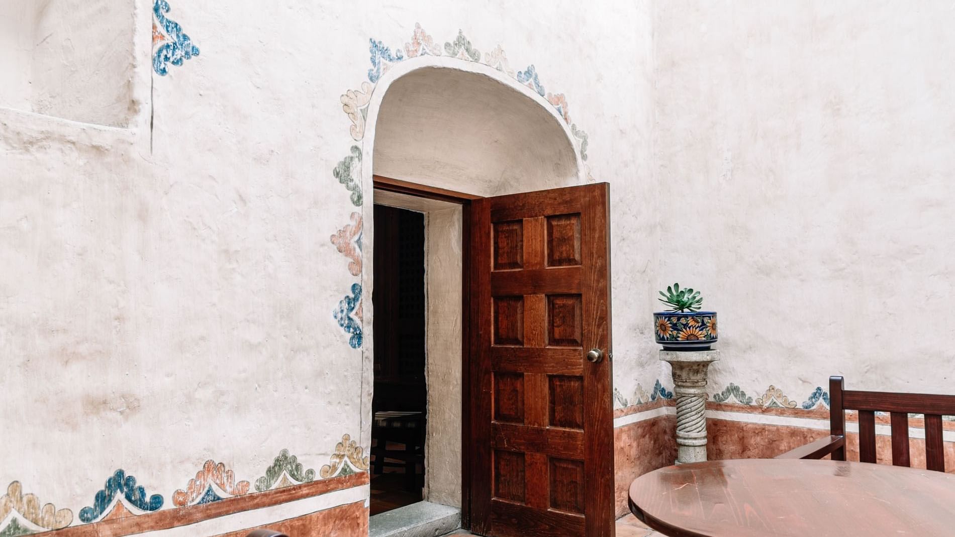 Wooden door slightly ajar in a white stucco wall, adorned with floral designs in King Governor Suite at Quinta Real Oaxaca