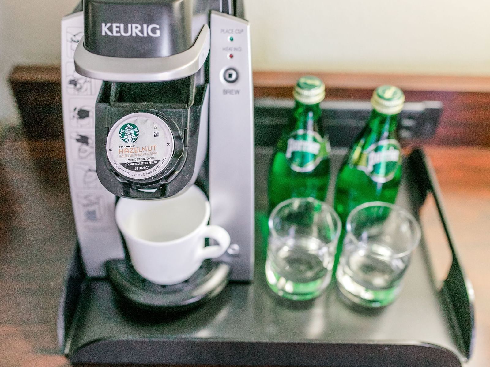 Keurig Coffee Maker with mug, Perrier water, and glasses on a tray.