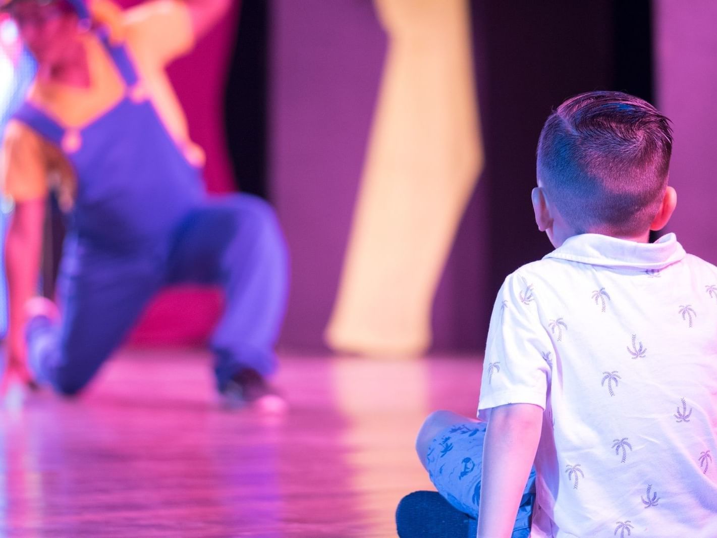 A kid sitting on the floor & enjoy a dance act at Fiesta Resort