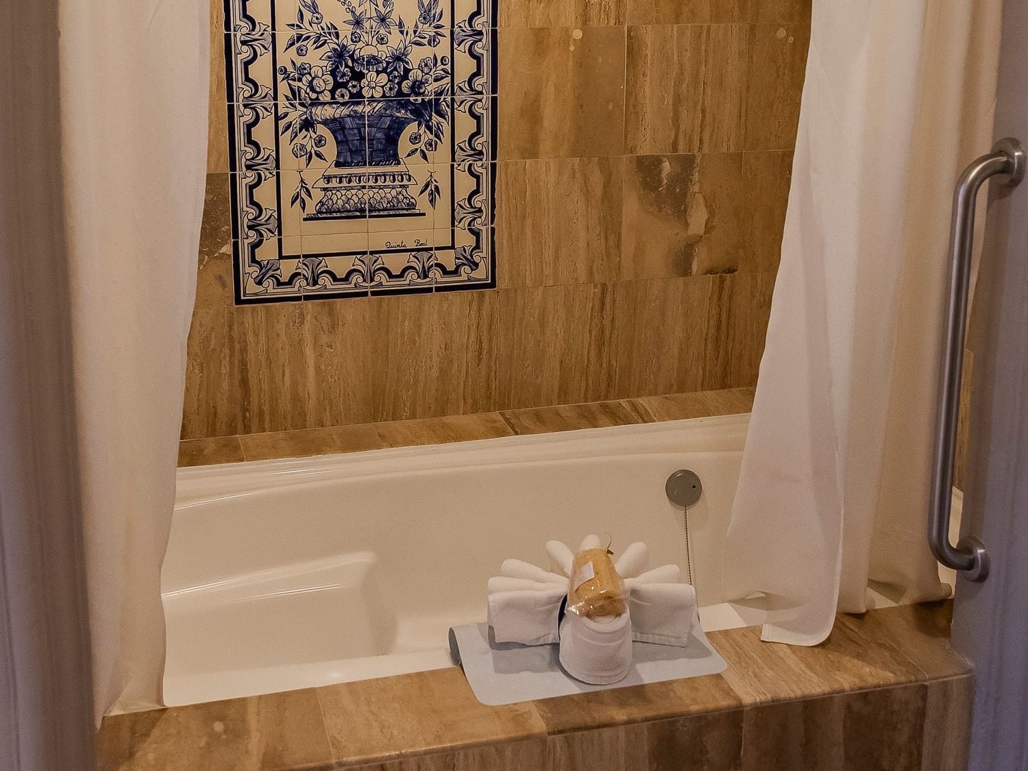 Elegant bathroom with white bathtub, wood-paneled walls, decorative tile art, and fresh towels at Quinta Real Zacatecas