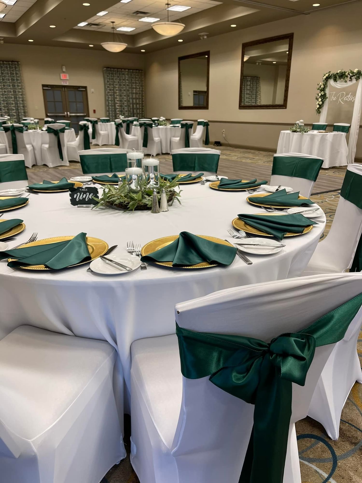 A formally set round table in a large meeting room with white and green decorations.