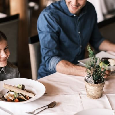 Two people dining at a table with gourmet dishes in restaurant at Falkensteiner Hotel Cristallo