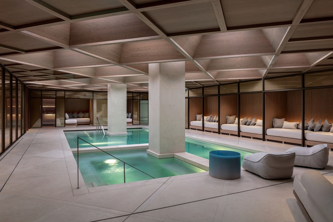 A serene indoor swimming pool area with modern design and lounging spaces at The Londoner Hotel's spa