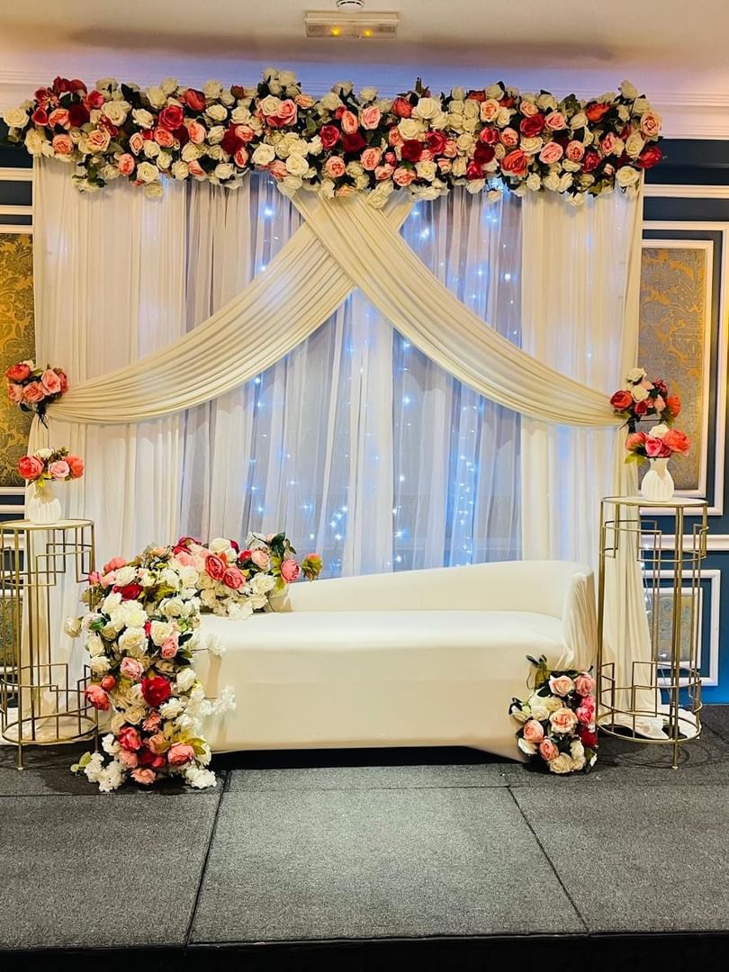 White chaise lounge by floral stands under a draped backdrop in the Blue Room at Warwick Doha