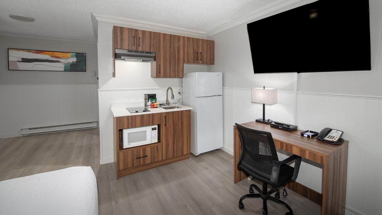 Kitchenette with microwave and fridge next to desk and TV.