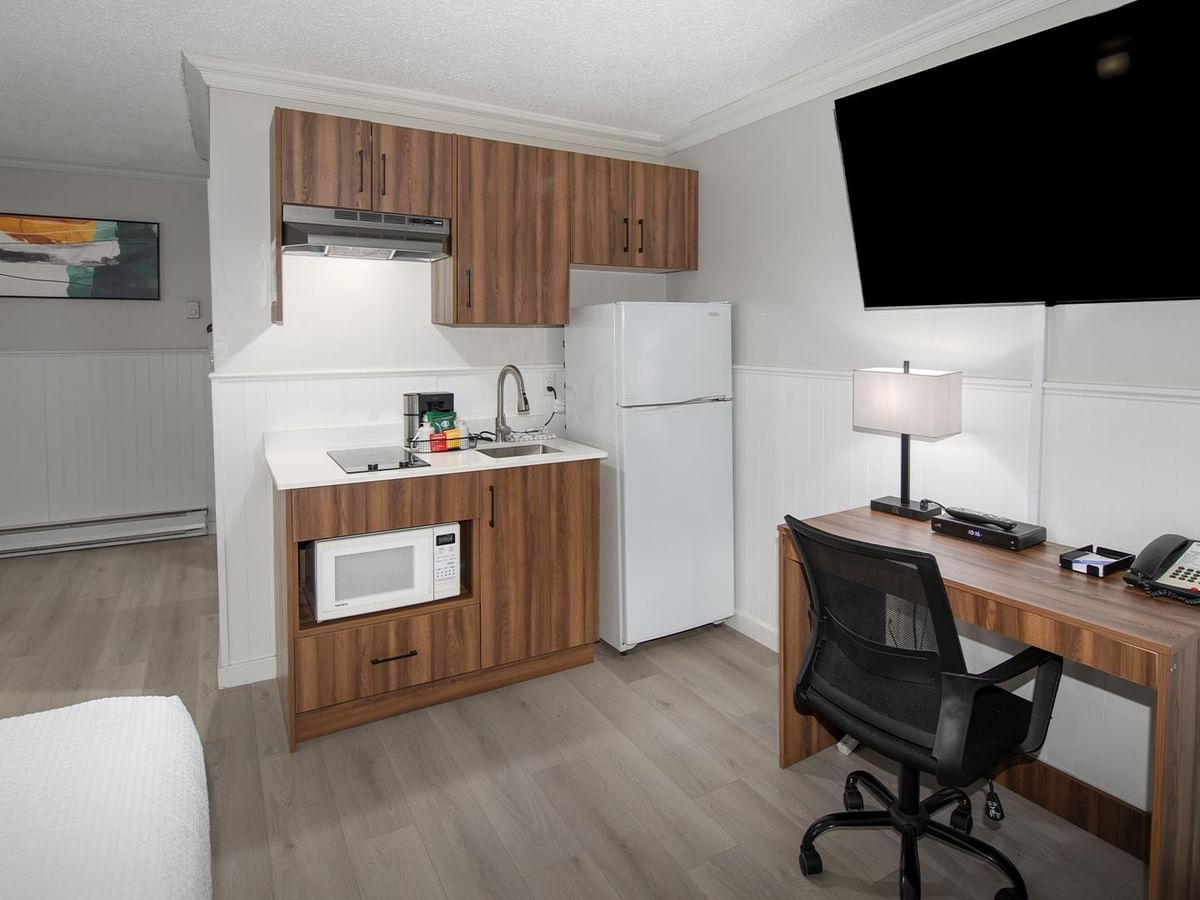 Room with Queen bed, kitchenette, work desk, and TV.