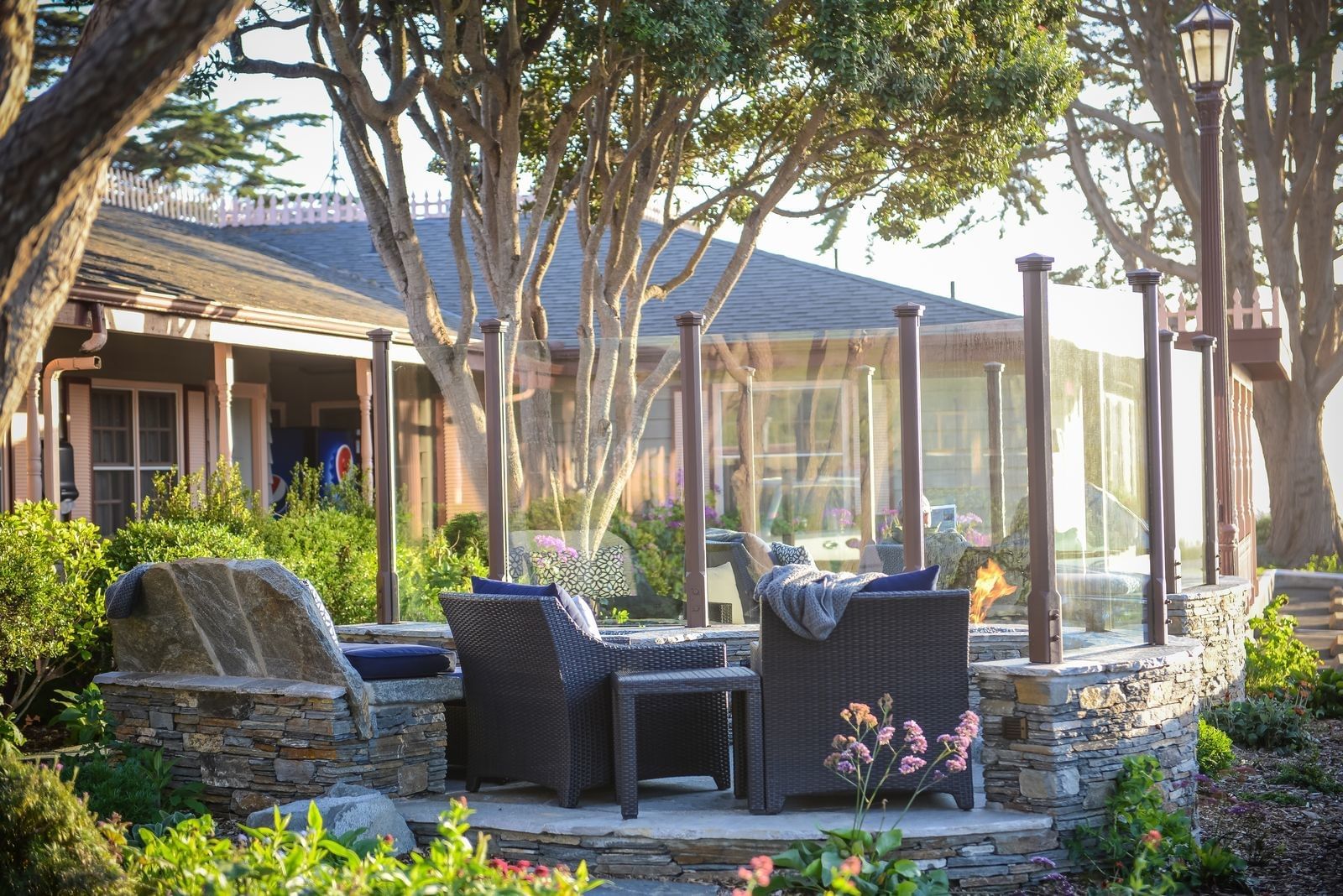 A cozy outdoor seating area with a stone fireplace, wicker furniture, and gardens.