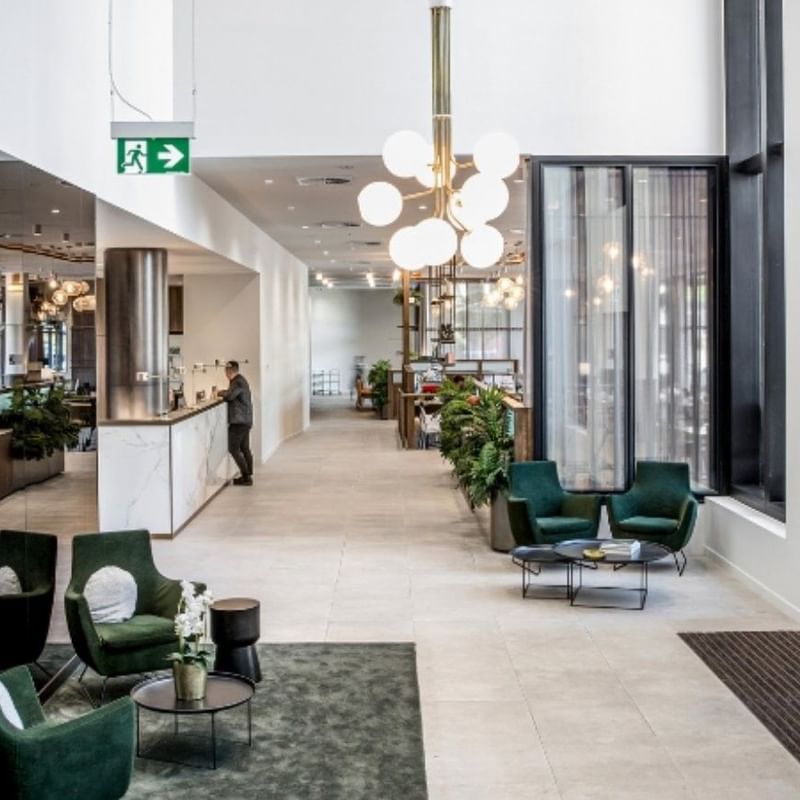 A modern BTR lobby with green chairs, a reception desk, and a chandelier over a seating area.