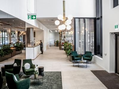 A modern BTR lobby with green chairs, a reception desk, and a chandelier over a seating area.