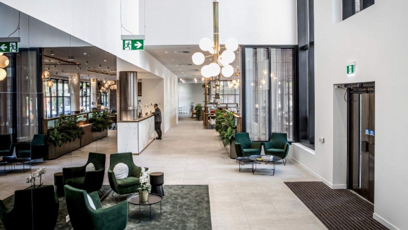 A modern BTR lobby with green chairs, a reception desk, and a chandelier over a seating area.