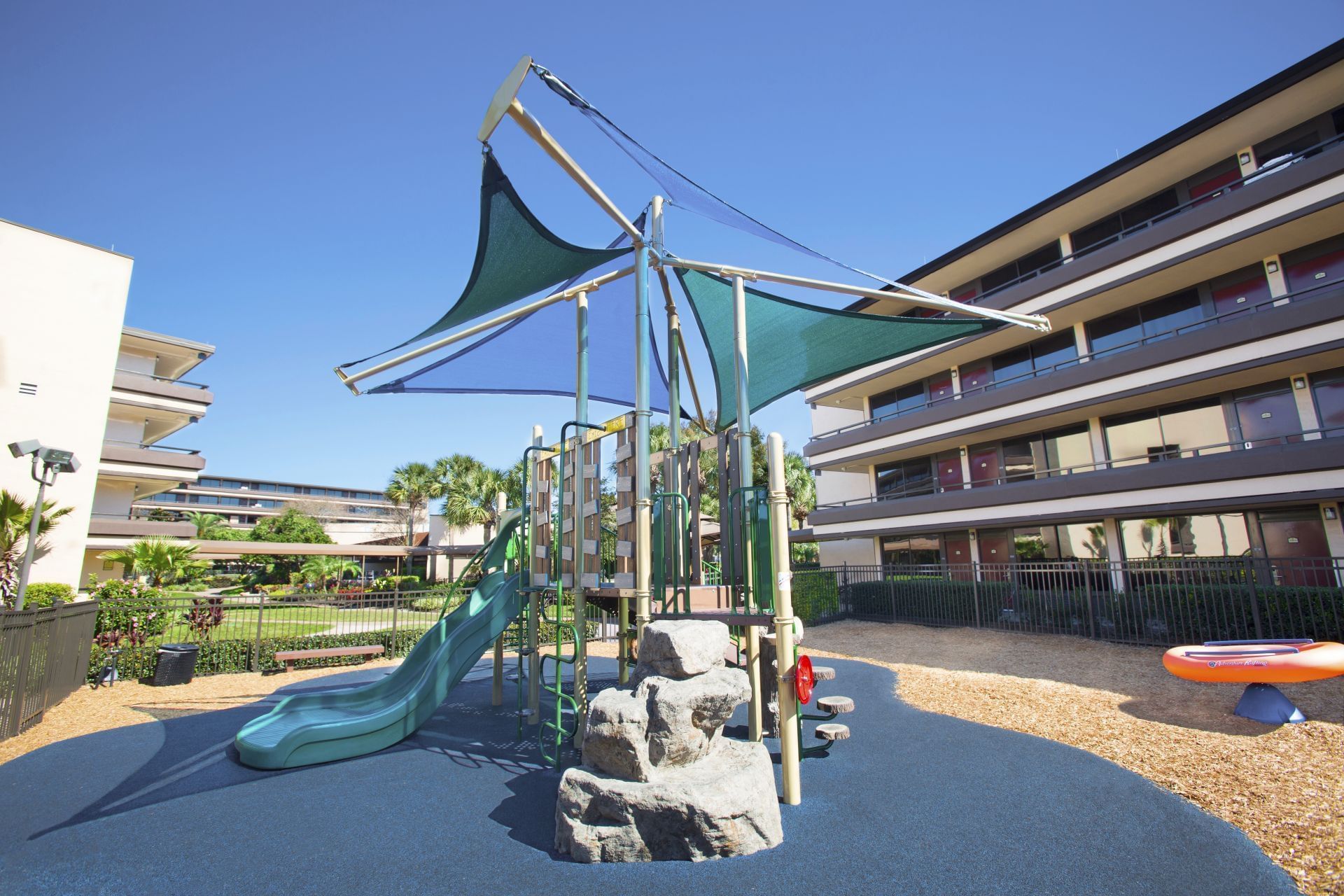 Children outdoor playground slide under shade canopy near guest buildings at Rosen Inn at Pointe Orlando
