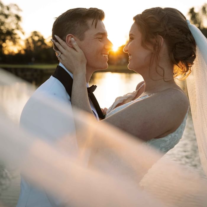 A bride and groom embracing at sunset by a lake near Mercure Kooindah Waters
