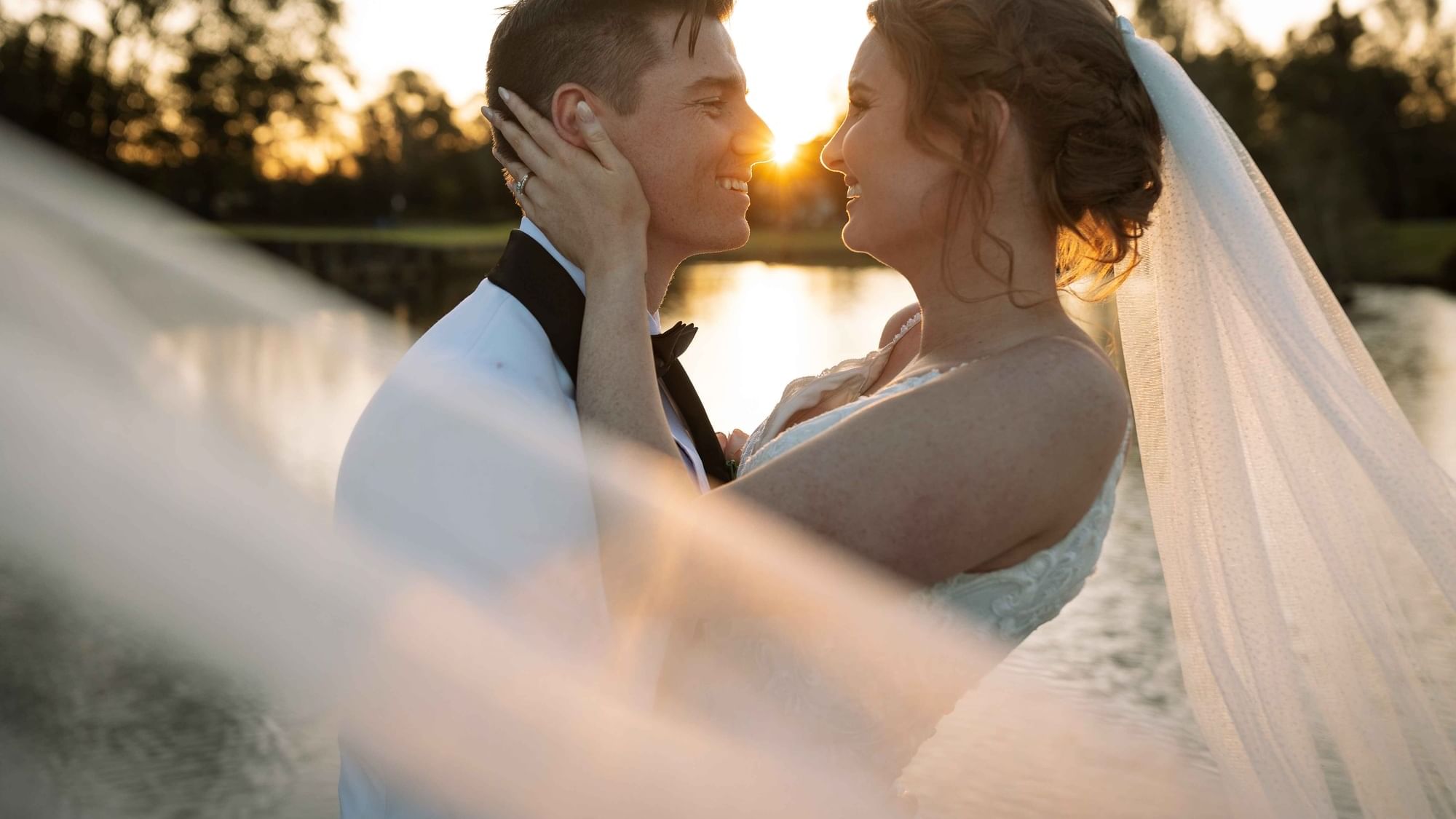A bride and groom embracing at sunset by a lake near Mercure Kooindah Waters
