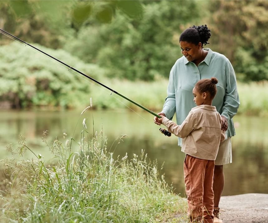 Side view of a Black mother teaching her daughter how to fish by a lake near Fall Creek Marina & Campground