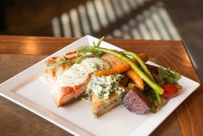 Salmon and scallops are on a white plate with carrots and asparagus, served at Hilltop Inn Salmon Arm