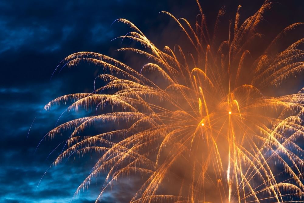 Golden fireworks explode against a dark blue sky.