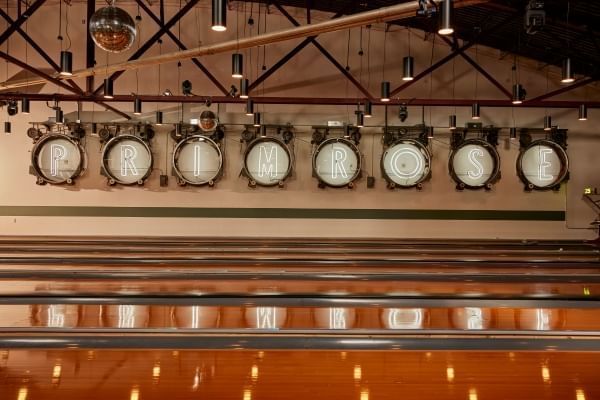 Lights reading ”Primrose” hang on a wall over shiny bowling lanes in a room with industrial lighting and disco balls. Primrose Lanes is a great spot for a romantic date in Orlando. 