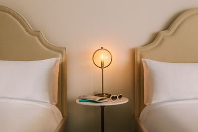 Room with two beds, a glowing brass lamp, sunglasses, and a magazine on a marble table at Kenmore Village Hotel South Beach