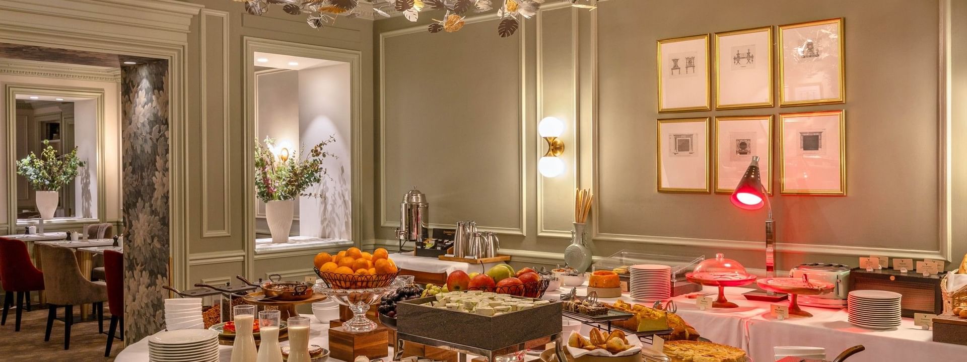 Breakfast spread with pastries and fruit on white linens under a leaf chandelier at Warwick Hotels & Resorts