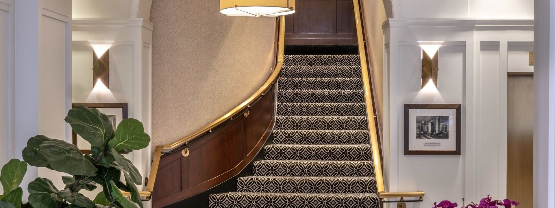 Grand staircase with patterned carpet by a wooden railing under a lamp at Warwick Allerton Chicago