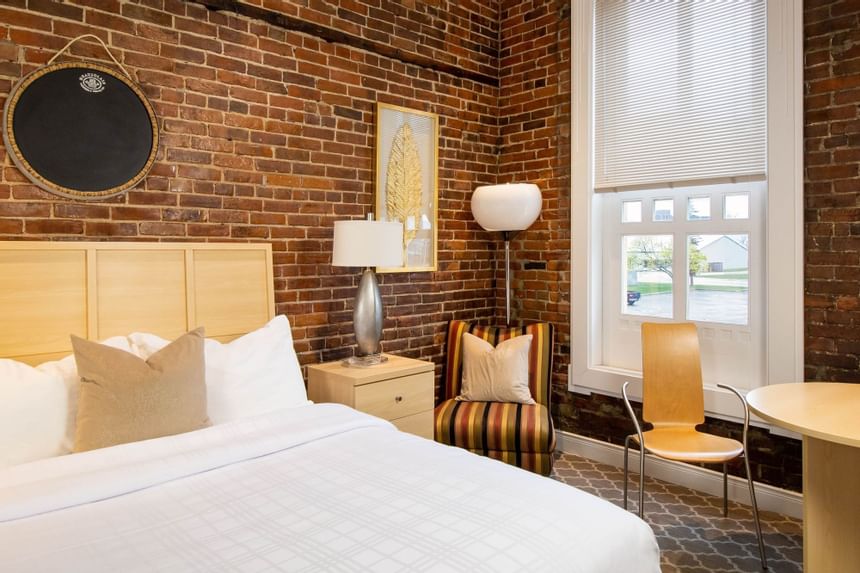 King bed, round table, brick wall & bedside cupboard with lamp in Queen Premiere Chardonnay at Retro Suites Hotel