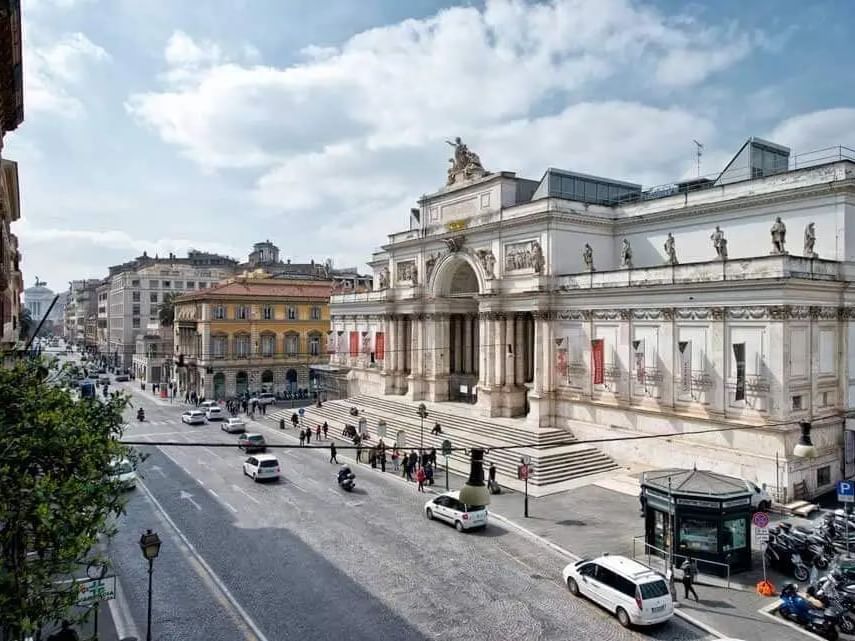 Bustling Via Nazionale with cars and pedestrians in front of a building under a cloudy sky near The Guardian Hotel