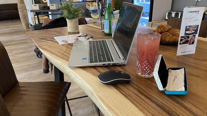 A laptop on a work desk with a juice at The Originals Hotels