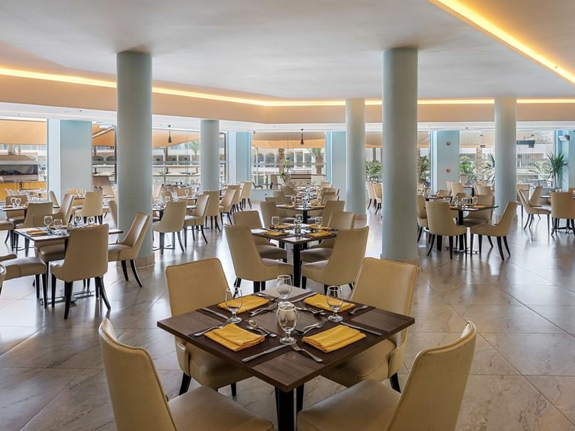 Spacious East and West restaurant with beige chairs, set tables, and modern lighting at Pickalbatros Royal Moderna Resort.