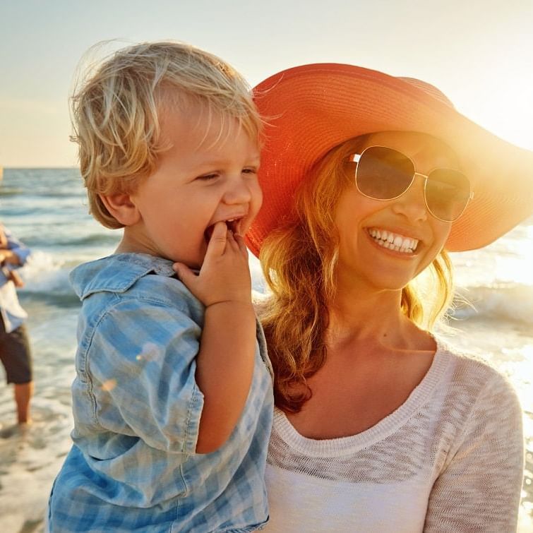 Mom and child smiling at the beach in the waves with dad and child in background