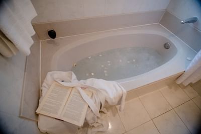 Soaking bathtub with open book and white bathrobe beside a glass of red wine at La Tourelle Hotel and Spa