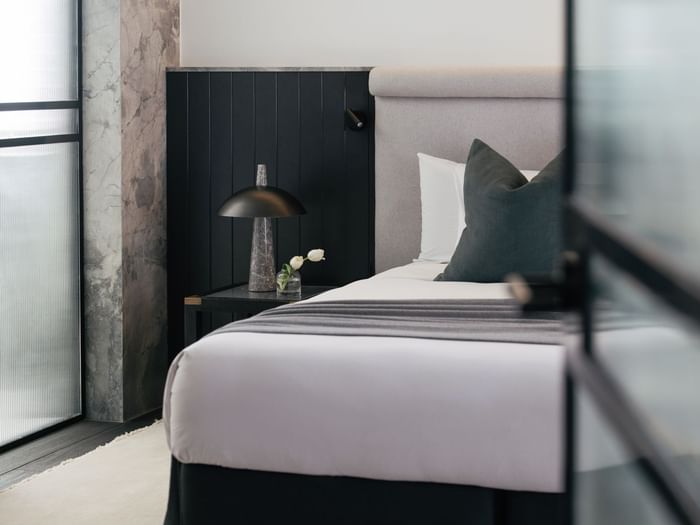 Elysium Suite at Elysium Manly with a black lamp and tulip vase by a wooden nightstand under a grey headboard