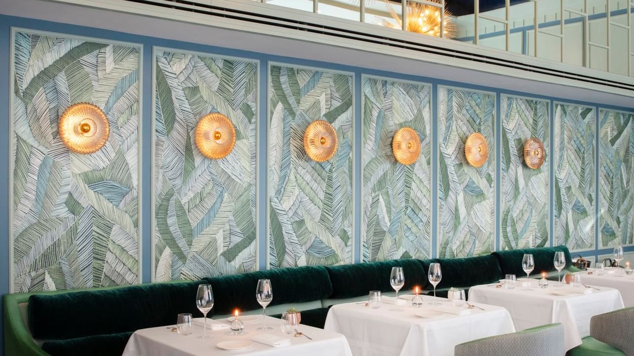 Dining area with a tropical leaf-patterned wall at Warwick Hotels and Resorts, with modern tables and seating