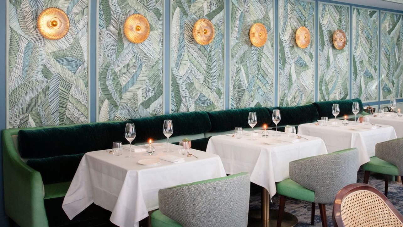 Decorated dining room with a tropical leaf-patterned wall at Warwick Hotels and Resorts, with modern tables and seating