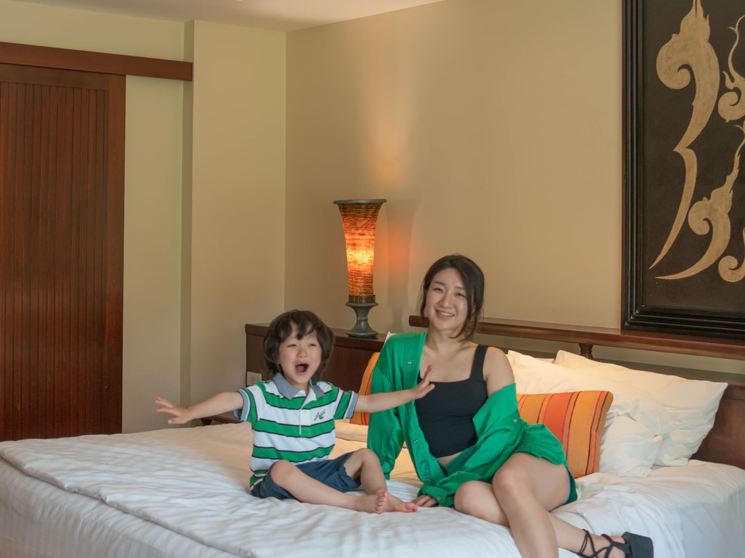 A mother and young child sitting on a king bed, smiling and enjoying their time together.