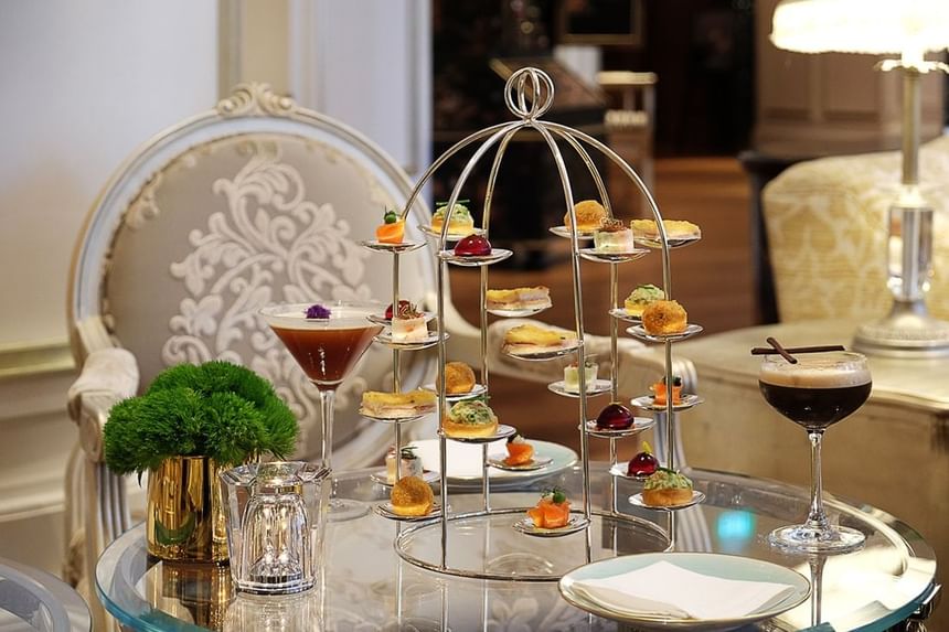 Elegant tiered stand with assorted gourmet snacks, flanked by two stylish cocktails in Park Lounge at Park Hyatt Saigon