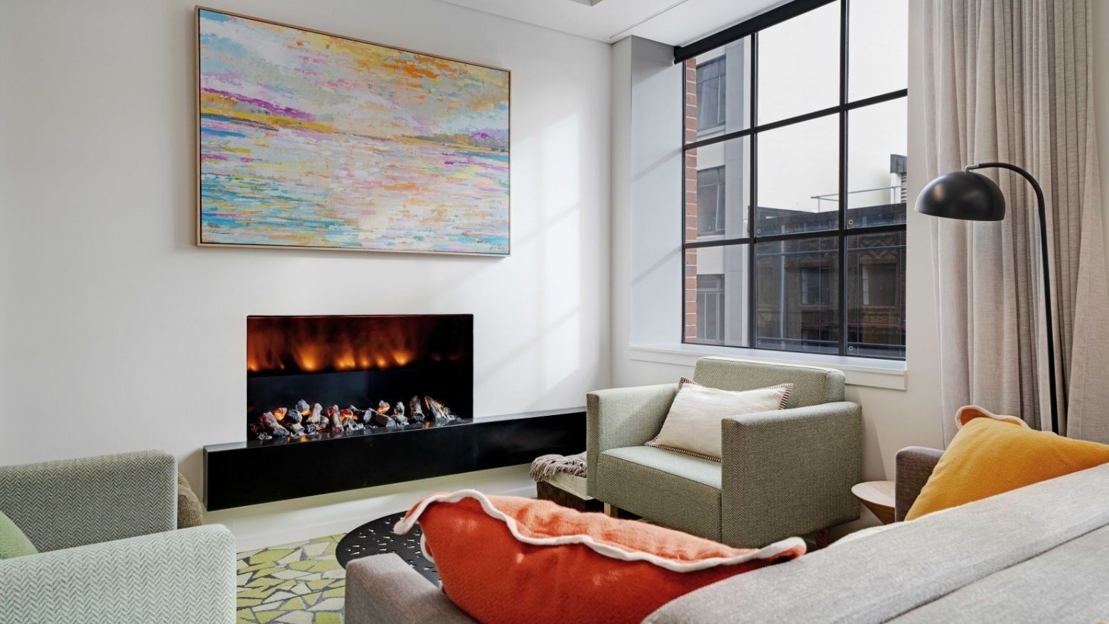 Modern living room with electric fireplace, colorful abstract art, and city view at UniLodge Auckland Central.