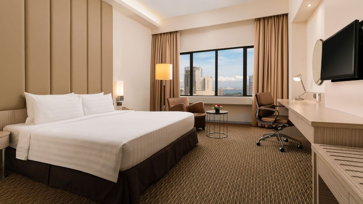 Work desk and cozy lounger by the bed in Premier King Room with city view and carpeted floors at Sunway Hotel Georgetown