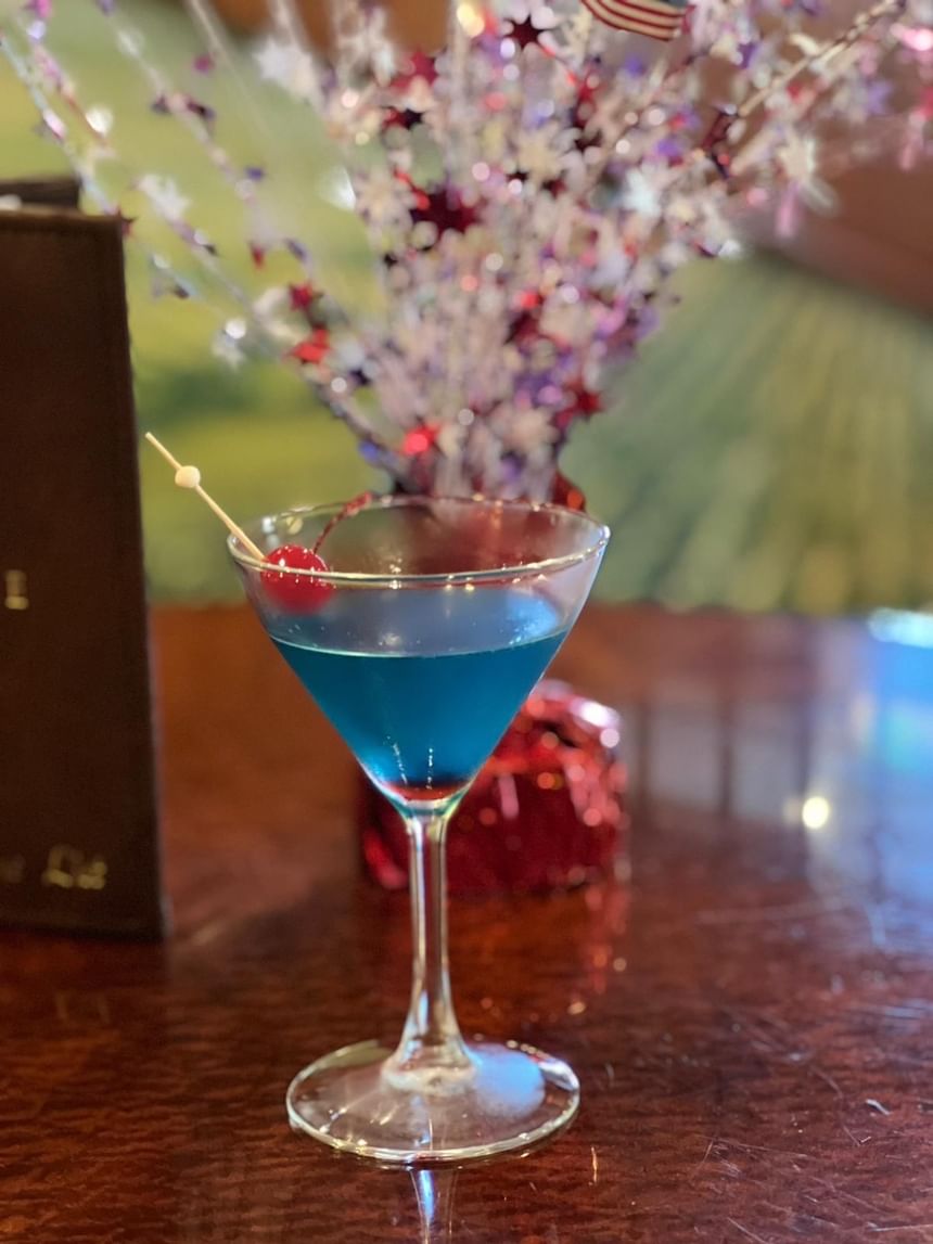 Vibrant blue cocktail served in a martini glass, garnished with a cherry at The Rose Hotel