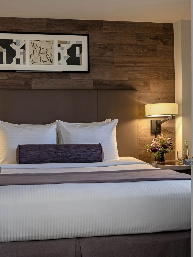 View through white french doors of a bed with a bolster by a bedside lamp in Premier Suite at Warwick Denver